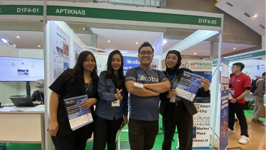 Empat staf Acoba berfoto di booth APTIKNAS sambil memegang brosur
